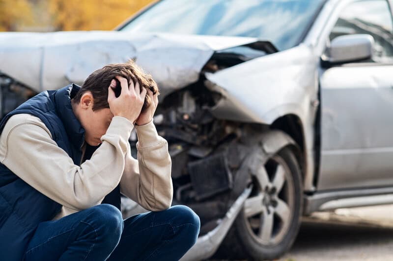 Man Sitting In Front Of His Totaled Car Stressed Out