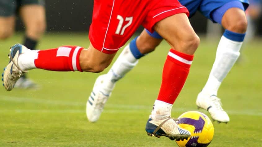 Athletes running after the soccer ball in a match.